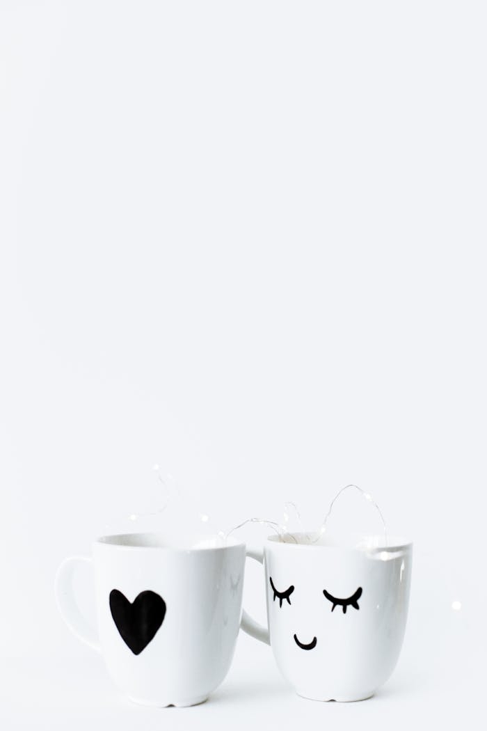 Two white mugs with heart and smiley face design against a light background.
